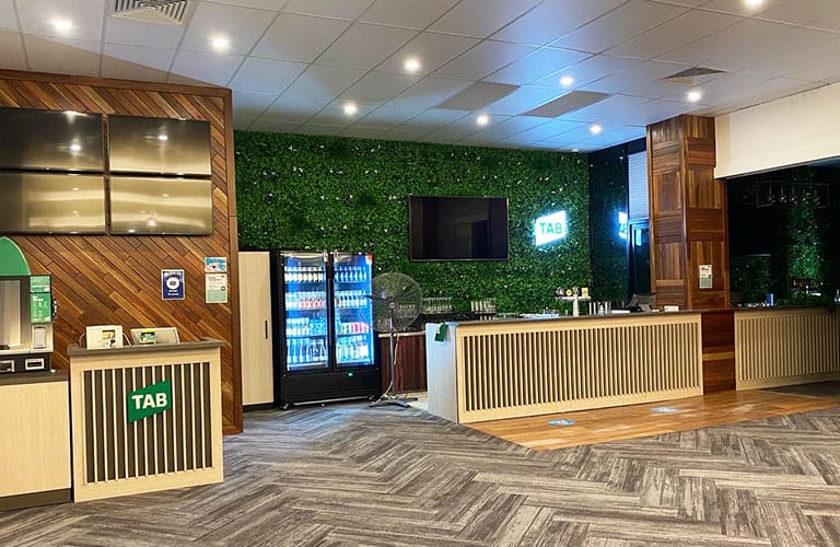 Hospitality refurbishment completed by Airey Building Group at the Gold Coast Turf Club, featuring a modern TAB service area with custom joinery, timber feature walls, decorative batten counters, artificial green wall and premium commercial finishes.