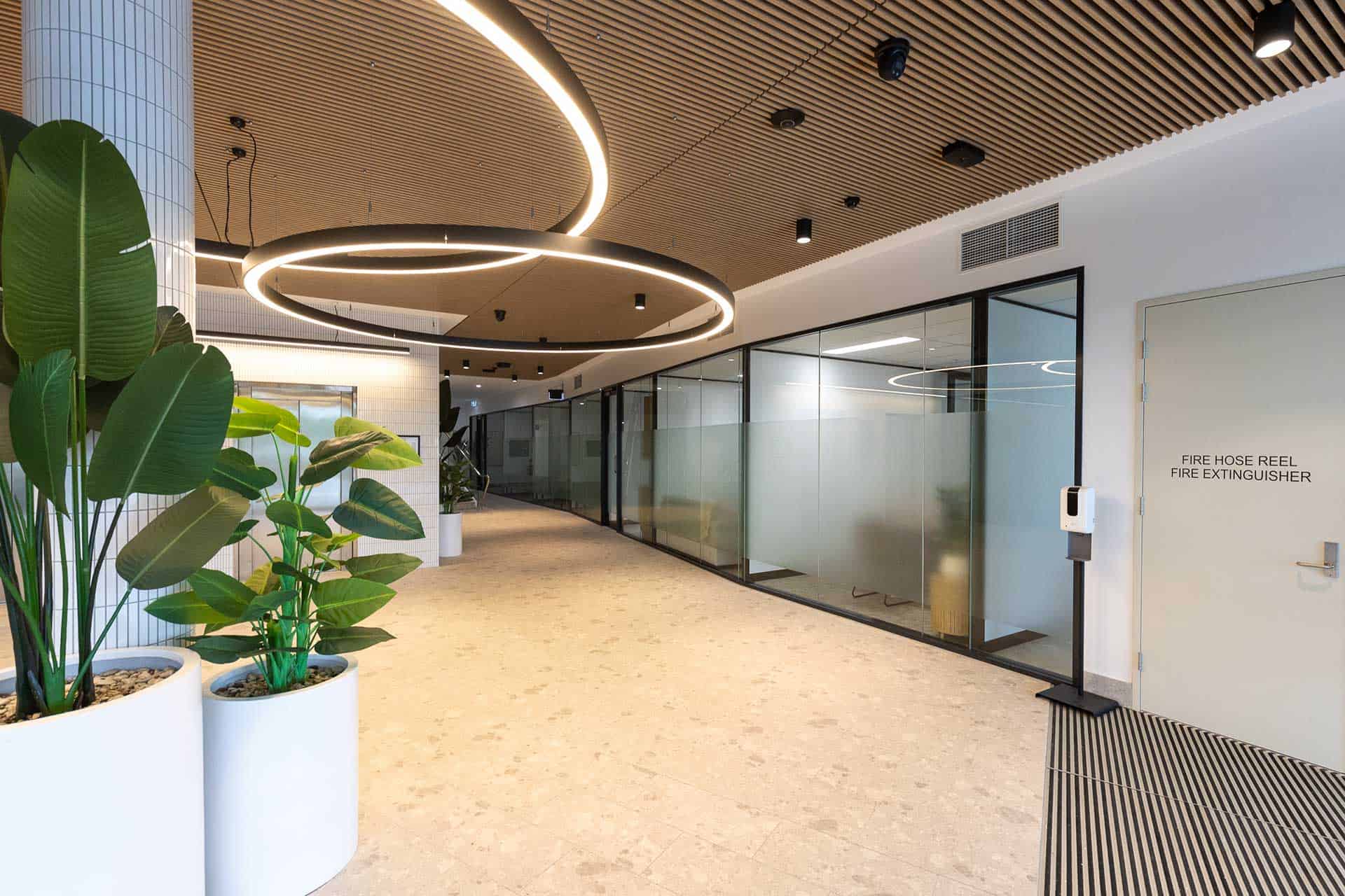 Premium commercial office fitout completed by Airey Building Group at M1 Business Hub, Helensvale, featuring feature timber batten ceilings, architectural ring lighting, glazed office suites, premium flooring and contemporary workplace design. M1 Business Hub Helensvale Commercial office fitout Helensvale Office fitout Gold Coast Commercial builder Helensvale Premium office fitout Workplace refurbishment Commercial office construction Business hub fitout Commercial interior fitout Custom office fitout Gold Coast commercial builder Airey Building Group