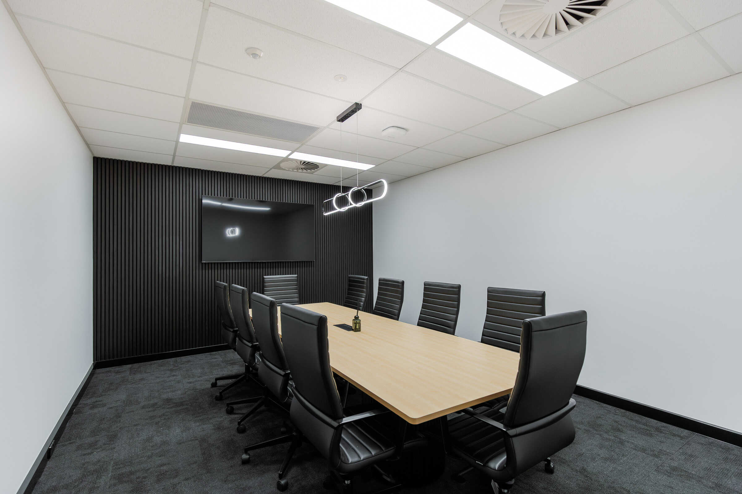 Modern commercial boardroom fitout completed by Airey Building Group at M1 Business Hub, Burleigh Heads, featuring a black timber batten feature wall, custom meeting table, architectural LED lighting and premium corporate finishes.